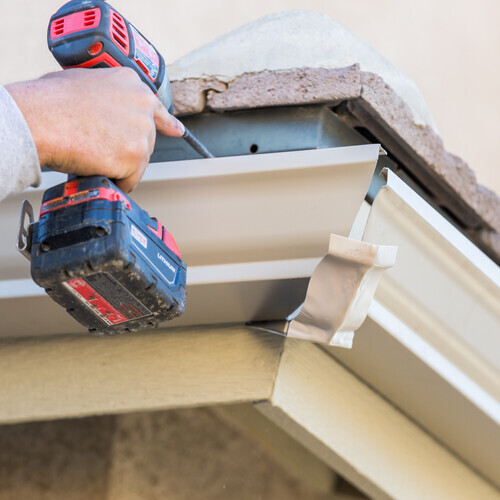 Worker Attaching Aluminum Rain Gutter to Fascia of House.